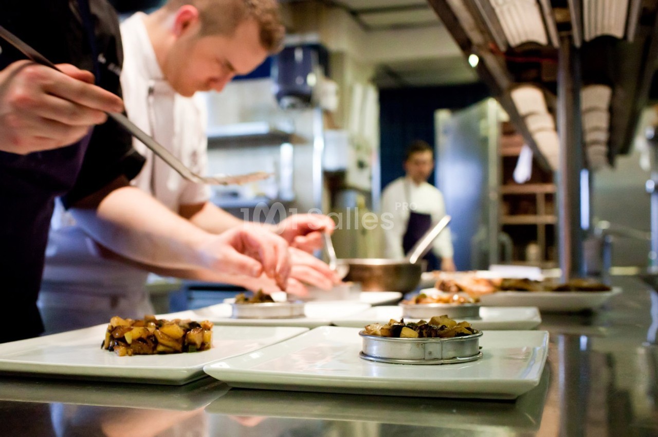 Des chefs préparent et dressent des plats dans une cuisine professionnelle.
