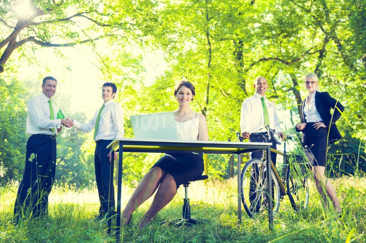 Un groupe de professionnels en tenue de bureau dans un parc, avec une femme assise à un bureau et un vélo à proximité.