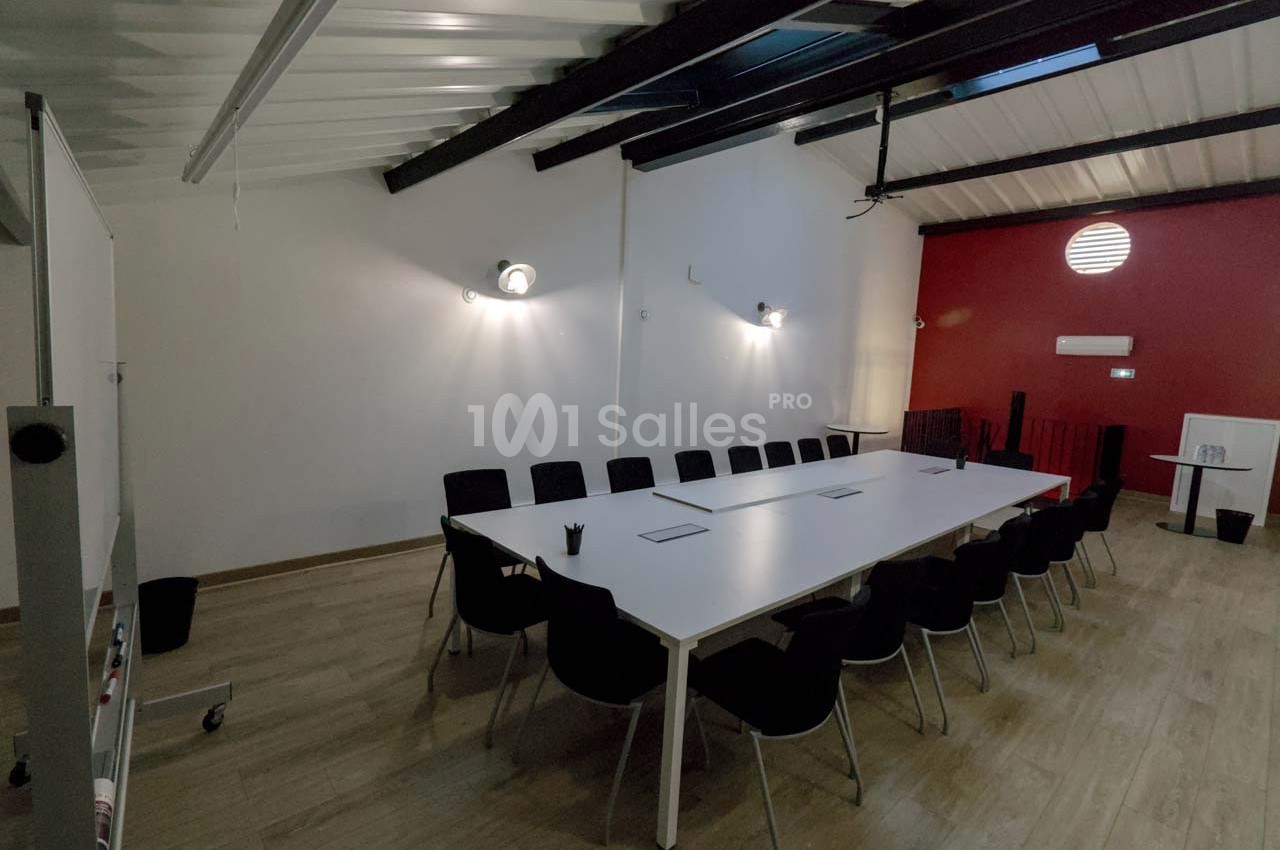 Salle de réunion moderne avec une grande table blanche entourée de chaises noires, éclairée par des appliques murales.