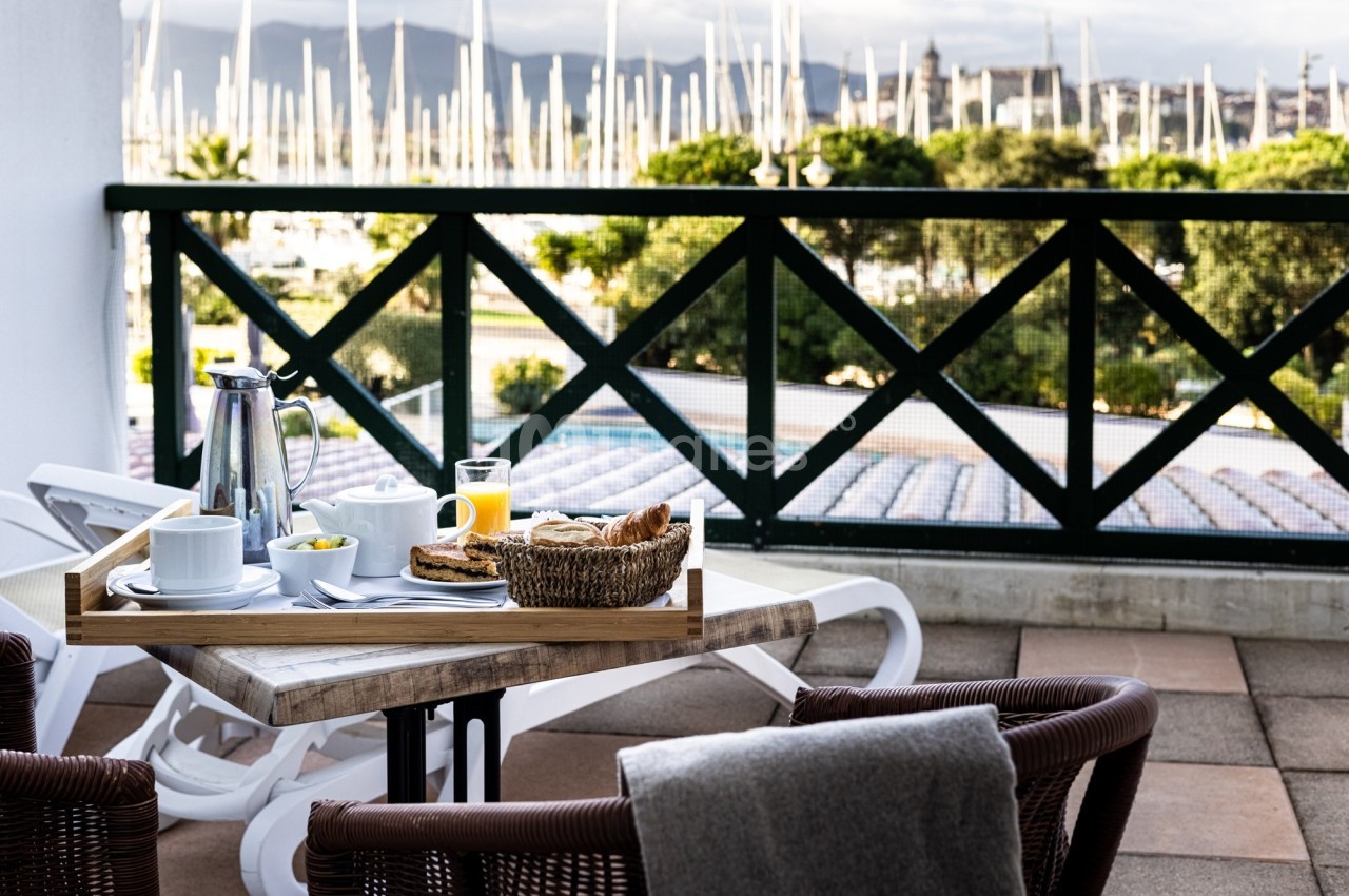 Petit-déjeuner servi sur une terrasse avec vue sur un port de plaisance et des voiliers à l'arrière-plan.