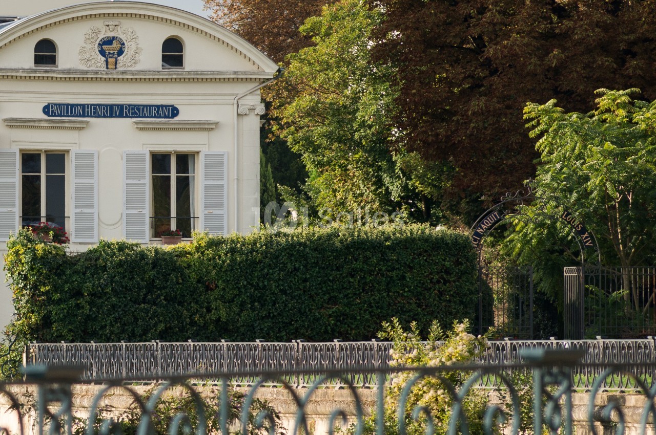 Façade d'un bâtiment blanc avec une enseigne ’Pavillon Henri IV Restaurant’, entouré de verdure et d'une clôture.