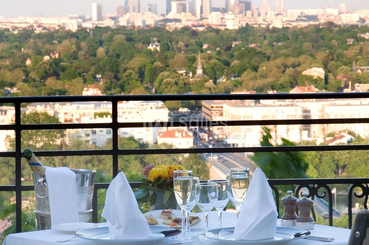 Table dressée avec élégance sur une terrasse, offrant une vue panoramique sur une ville entourée de verdure.