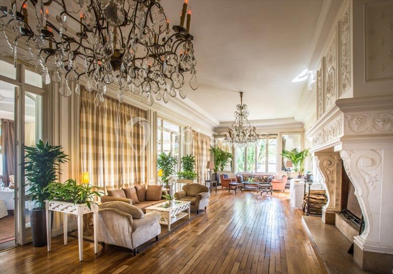 Salon spacieux avec parquet en bois, cheminées sculptées, lustres en cristal et grandes fenêtres laissant entrer la lumière.
