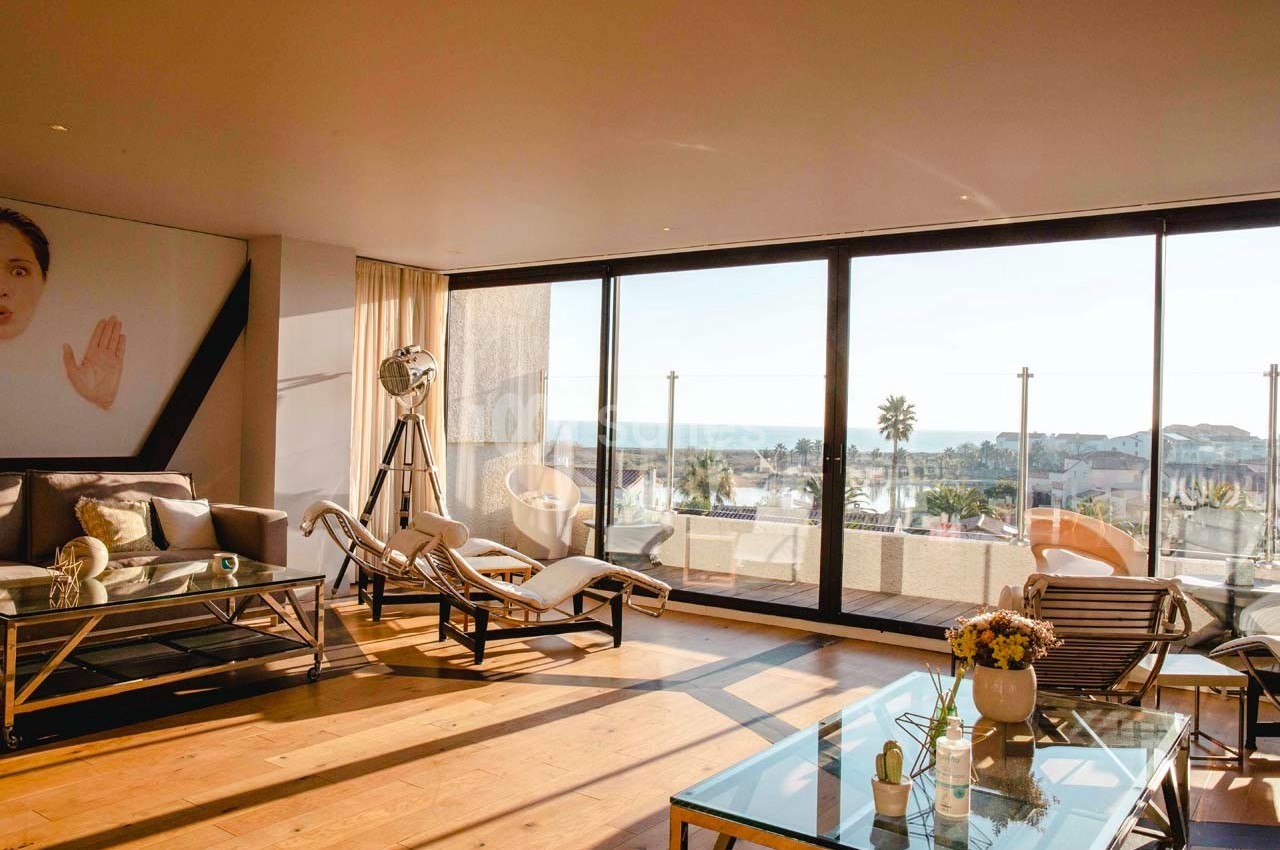 Salon lumineux avec grandes baies vitrées donnant sur une terrasse et vue sur la mer, décoré avec mobilier moderne.