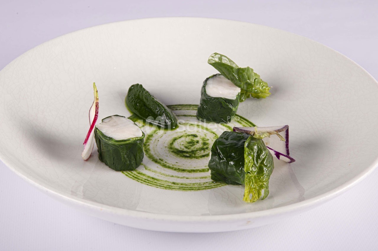 Assiette contenant des rouleaux de légumes verts garnis, accompagnés de feuilles, radis et sauce verte décorative.