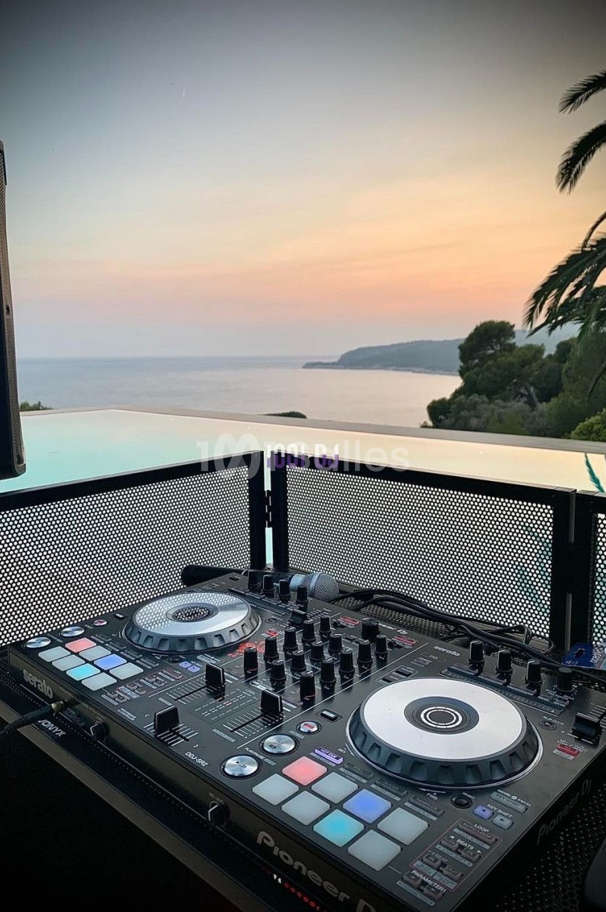 Table de mixage DJ installée en extérieur avec vue sur la mer au coucher du soleil.