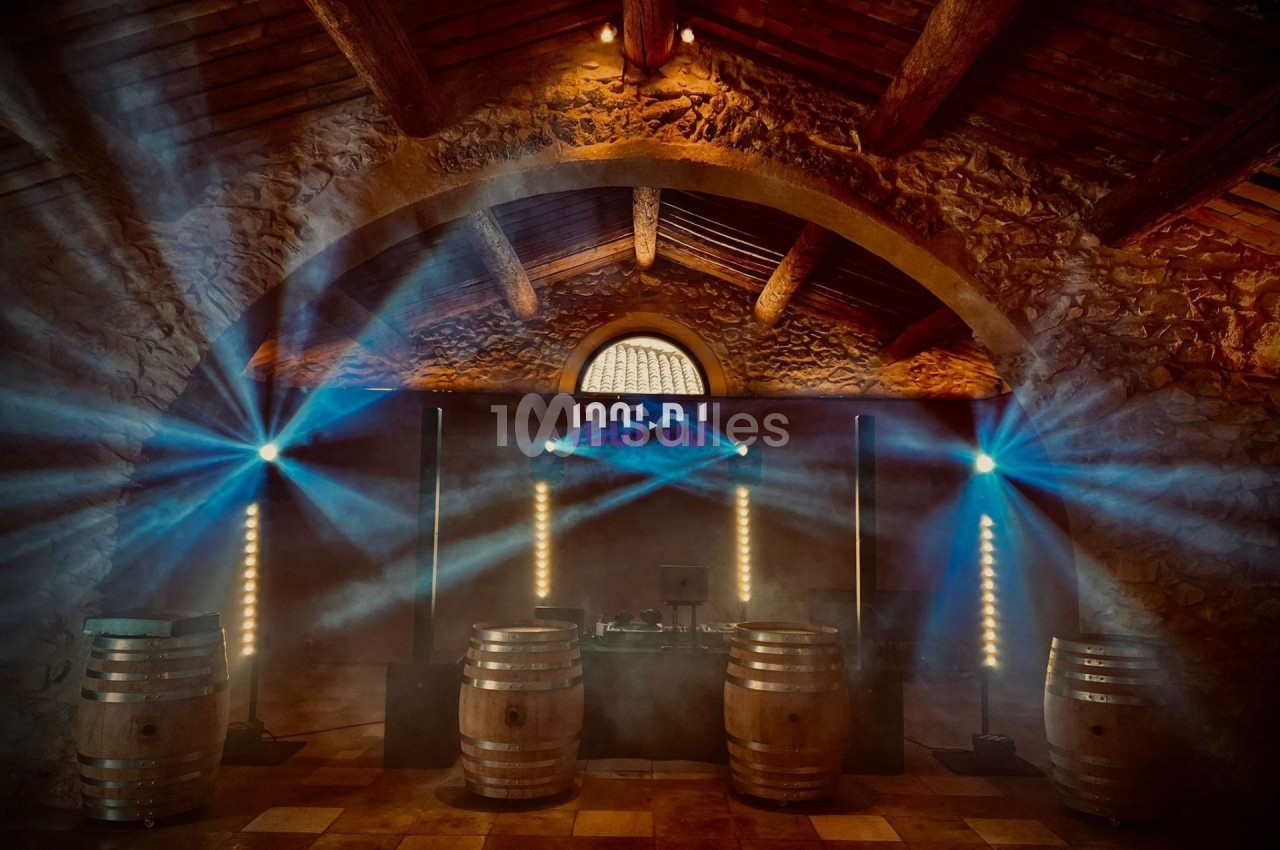 Salle voûtée en pierre avec éclairage coloré, barriques en bois et équipement de sonorisation au centre.