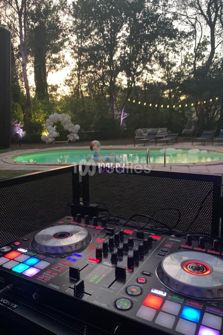 Table de mixage éclairée au premier plan, avec une piscine et un jardin en arrière-plan au crépuscule.
