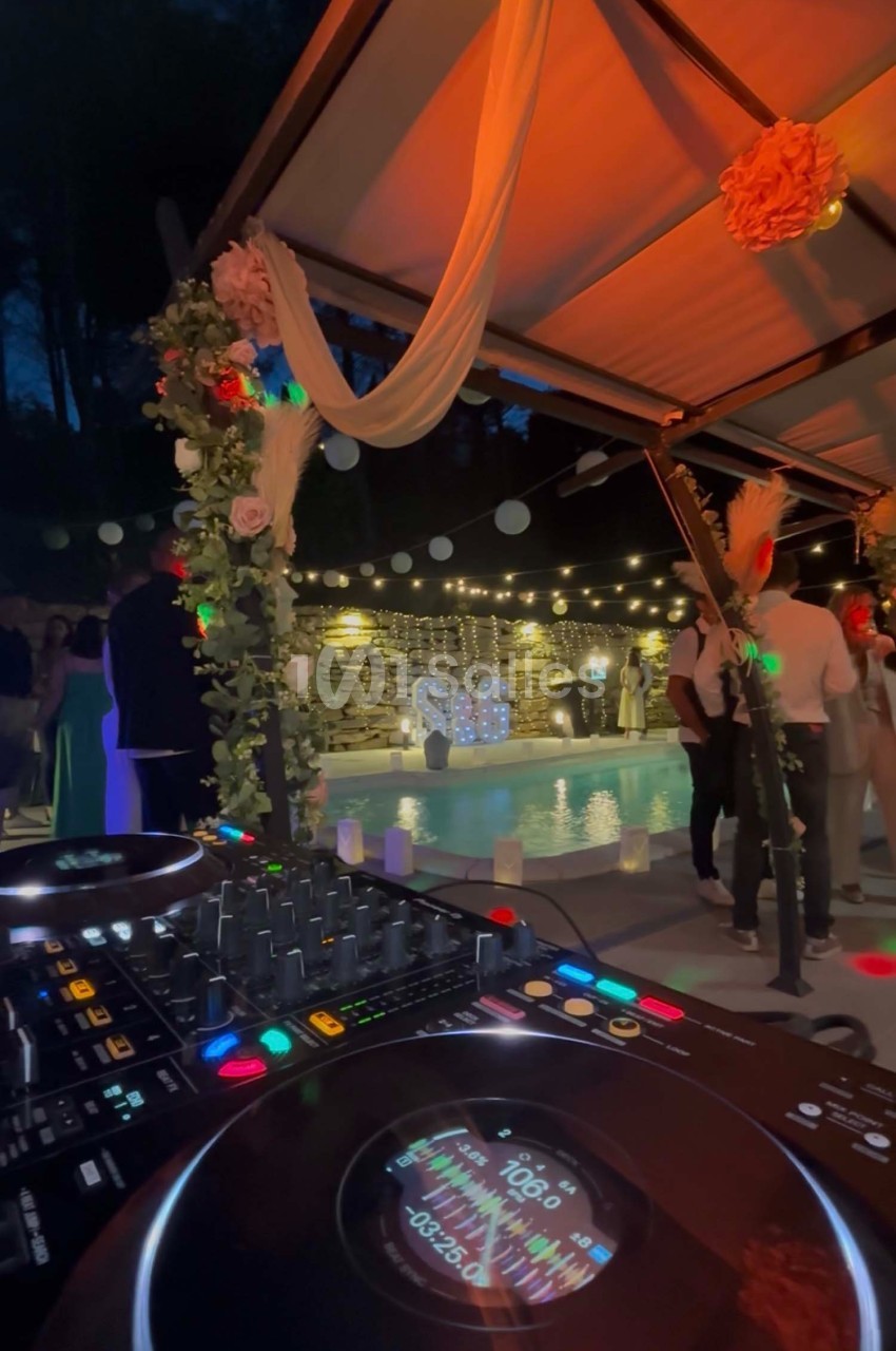 Table de mixage en premier plan lors d'une soirée en extérieur avec des invités dansant sous une pergola décorée.