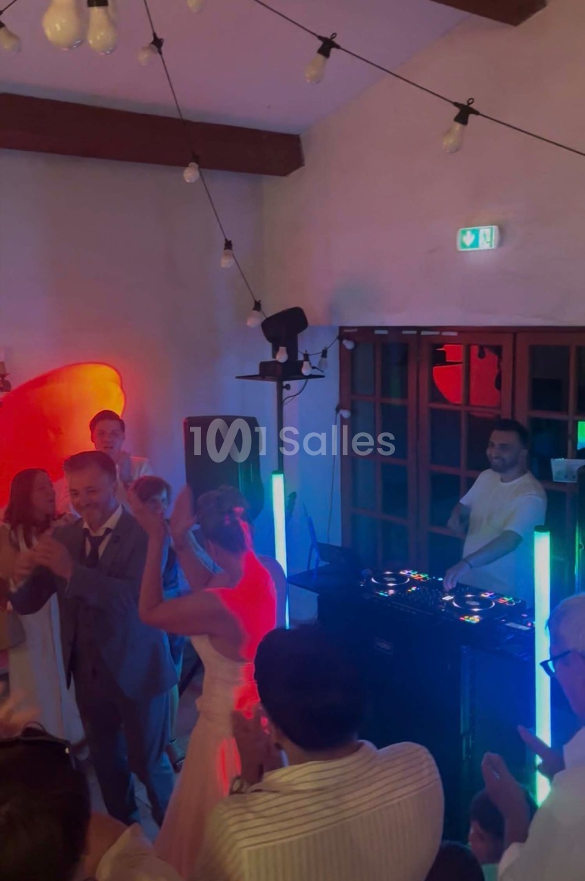 Des invités dansent autour d'un DJ lors d'une fête dans une salle éclairée par des lumières colorées.