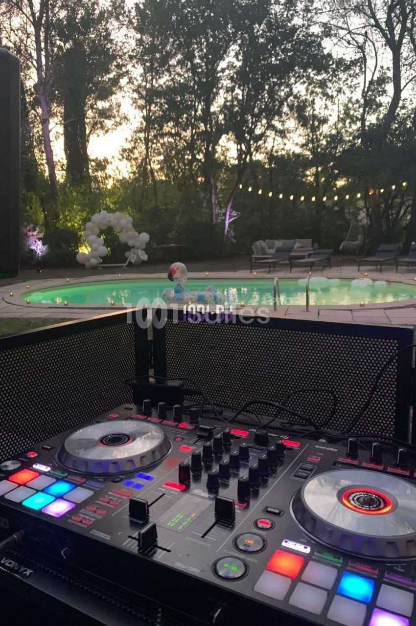 Table de mixage éclairée au premier plan, avec une piscine et un jardin en arrière-plan au crépuscule.