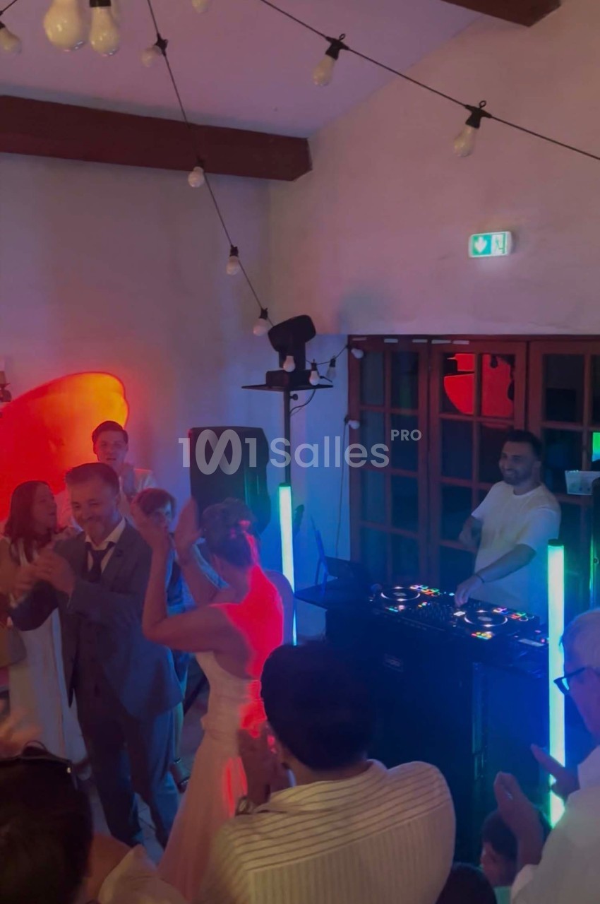 Des invités dansent autour d'un DJ lors d'une fête dans une salle éclairée par des lumières colorées.
