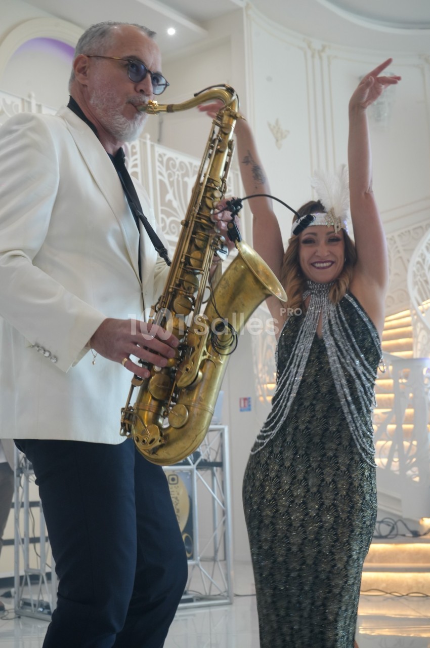 Un musicien jouant du saxophone accompagné d'une femme souriante dansant dans un décor élégant.