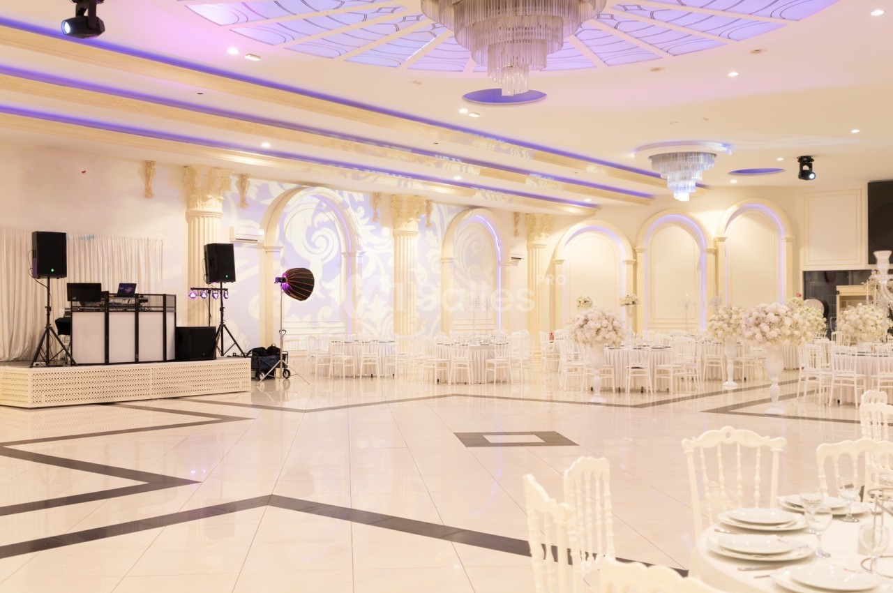 Salle de réception élégante avec tables dressées, chaises blanches et piste de danse, éclairage lumineux et décor raffiné.