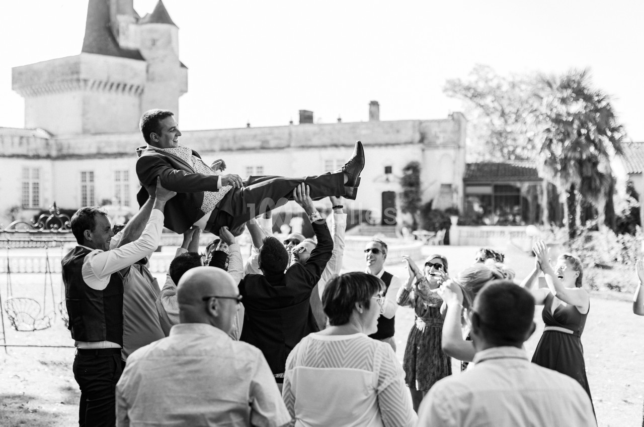 Un homme en costume est soulevé par un groupe de personnes lors d'une célébration en extérieur devant un château.