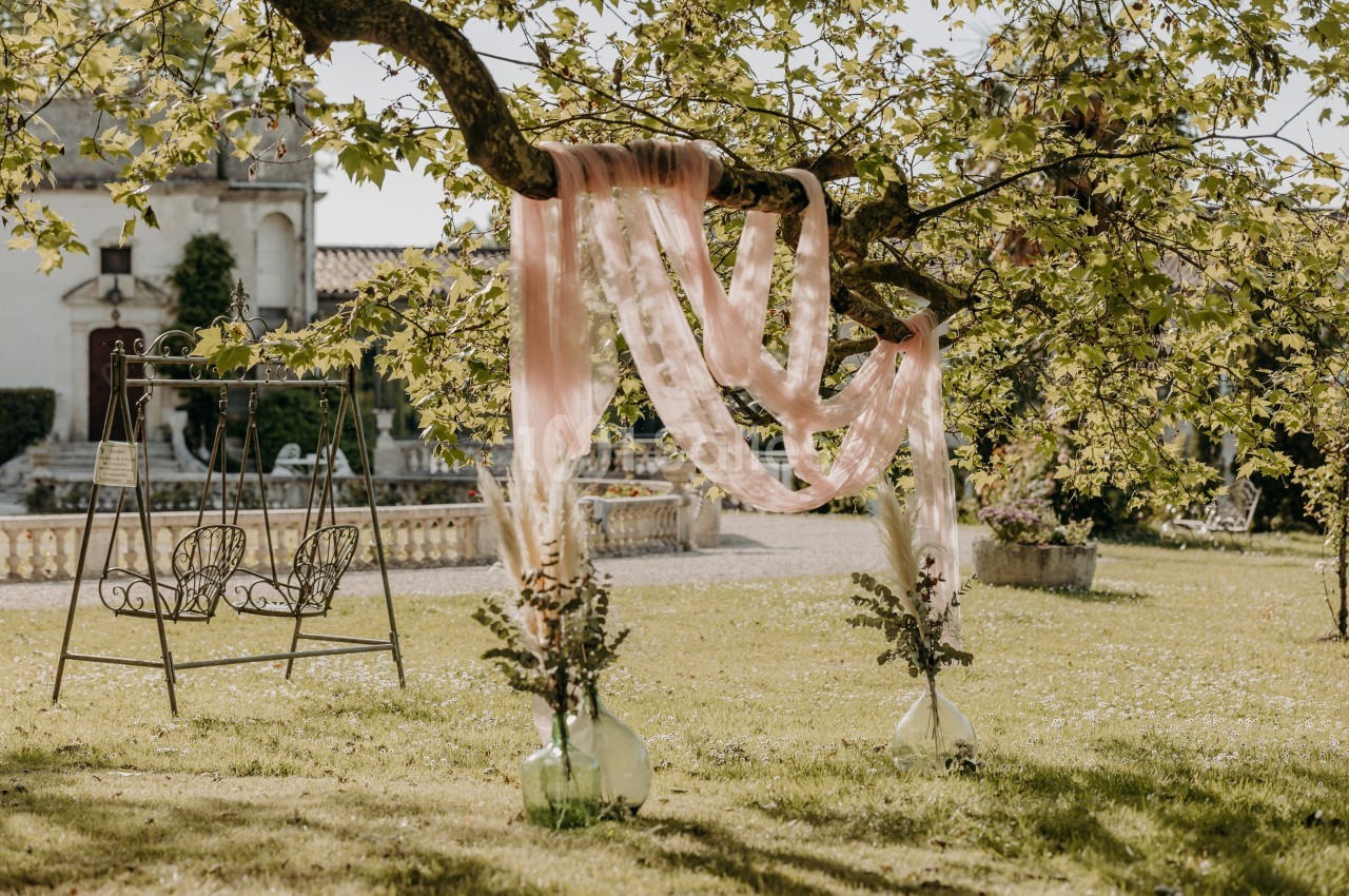 Tissu rose suspendu à une branche d'arbre dans un jardin, avec une balançoire et des vases décoratifs au sol.