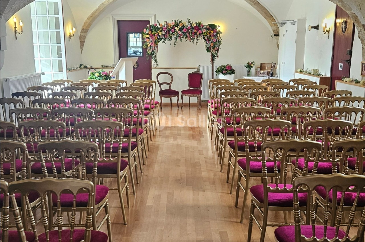 Salle de cérémonie avec des chaises dorées à assise rouge, un autel fleuri et une arche décorative en arrière-plan.