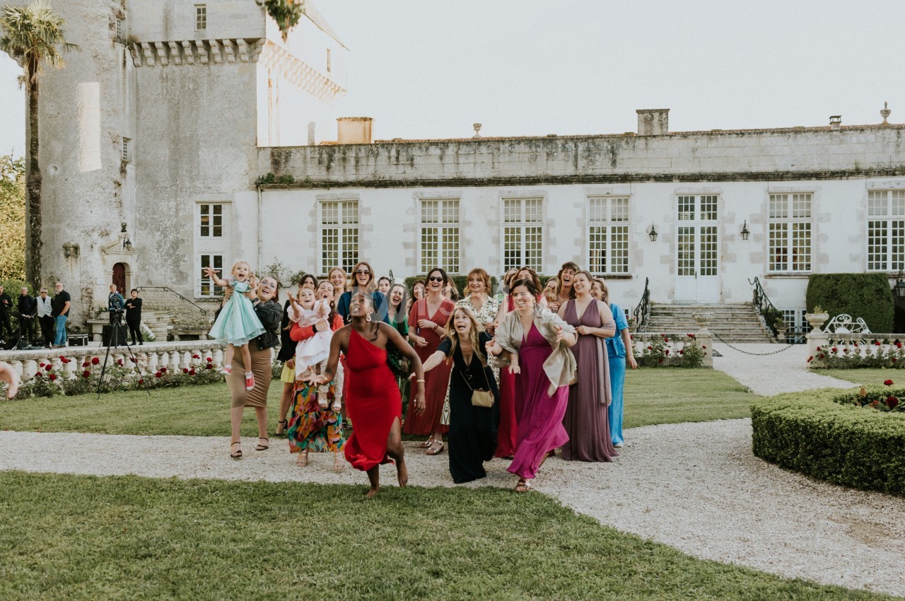 Un groupe de femmes élégamment vêtues marche joyeusement dans un jardin devant un bâtiment historique.