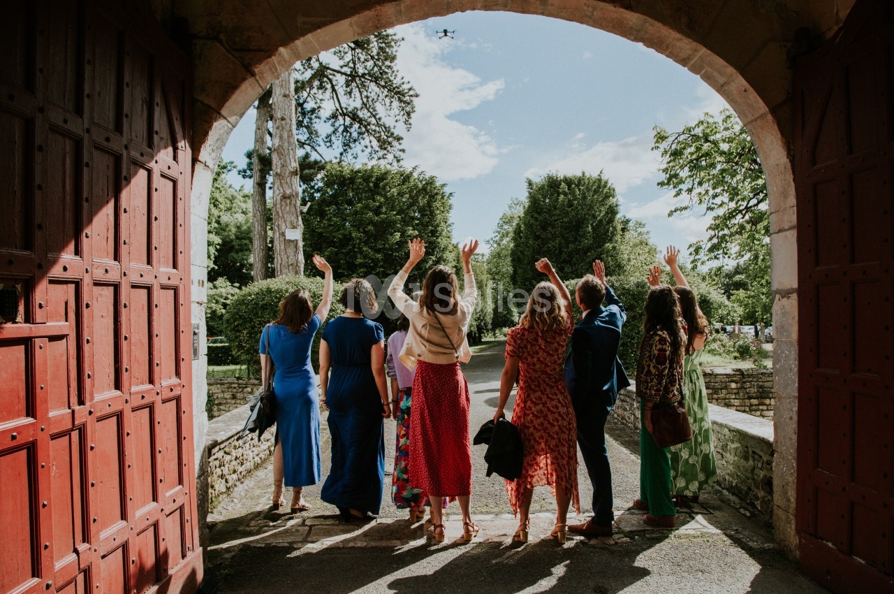 Un groupe de personnes saluant de la main sous une arche en bois rouge, avec un jardin en arrière-plan.
