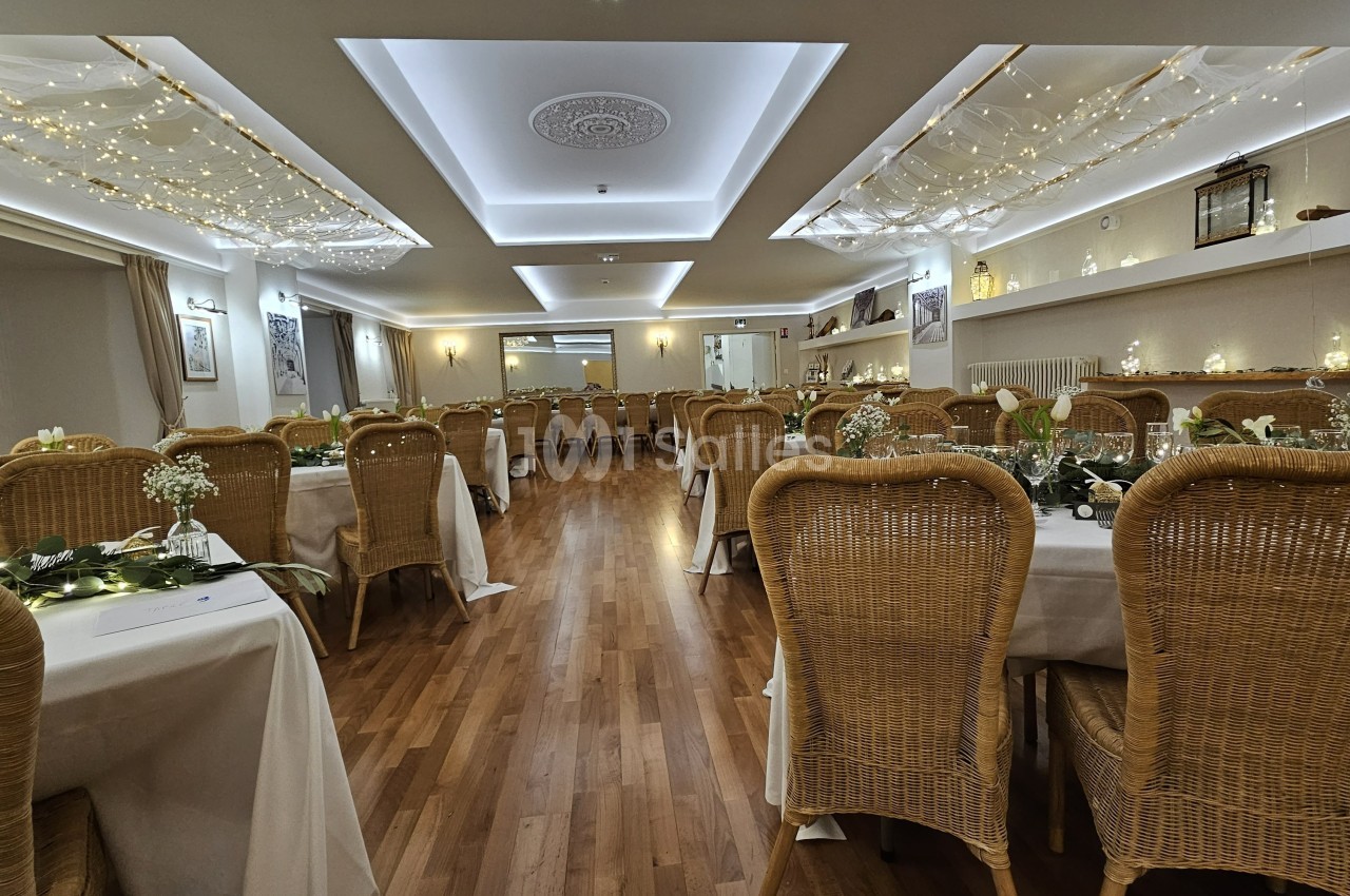 Salle de réception décorée avec des guirlandes lumineuses, des tables dressées et des chaises en rotin.