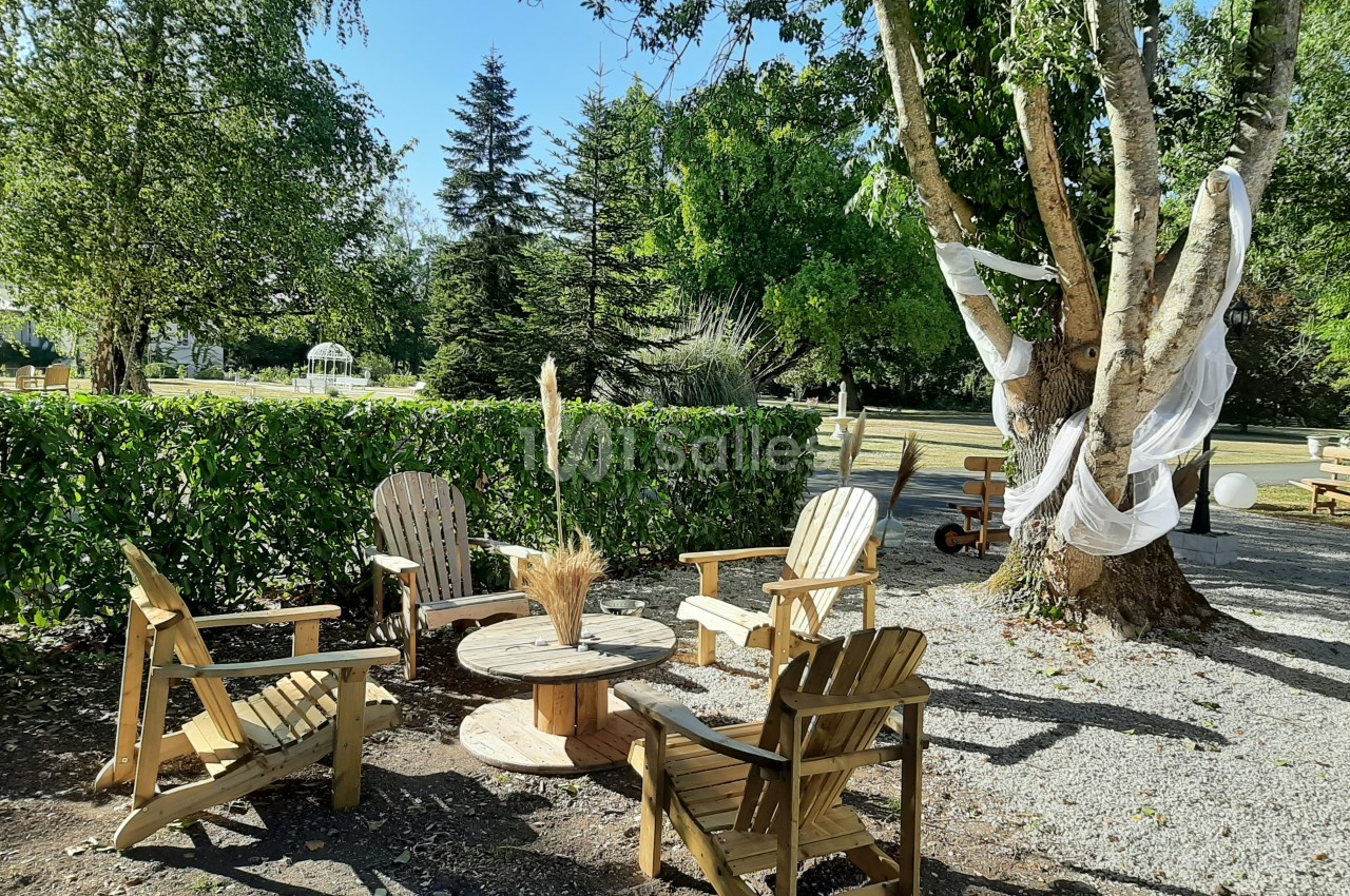 Quatre chaises en bois disposées autour d'une table basse en extérieur, sous des arbres avec des décorations en tissu.