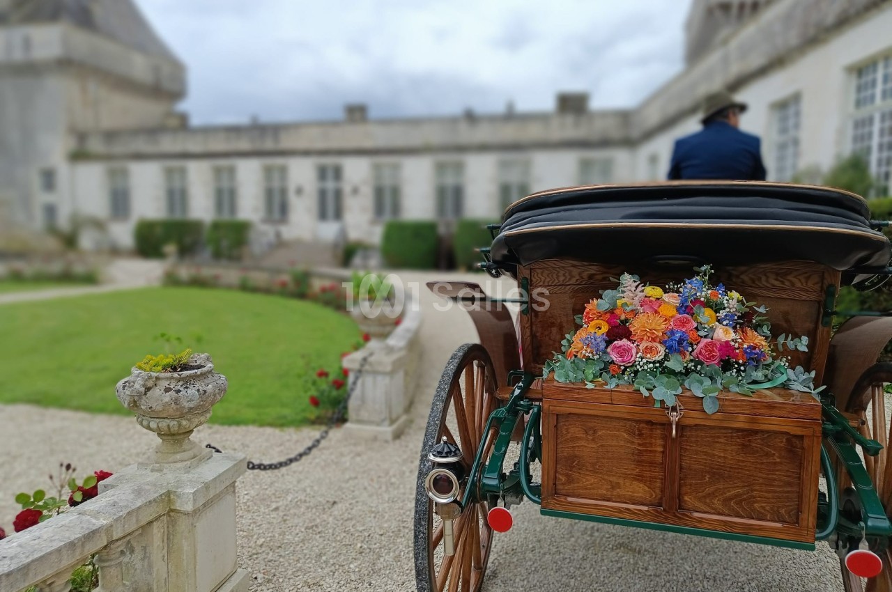 Calèche décorée de fleurs colorées stationnée dans une cour pavée devant un bâtiment ancien.