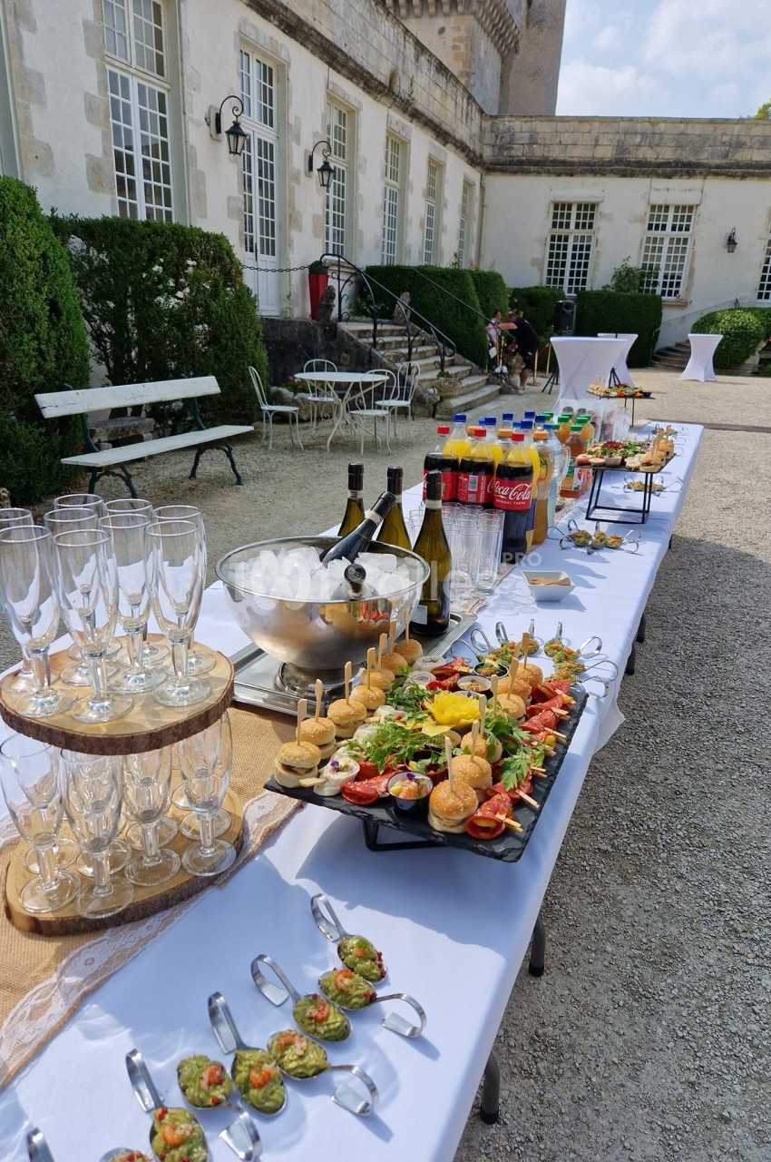 Buffet en extérieur avec verrines, amuse-bouches, boissons et coupes de champagne, disposés sur une table blanche.