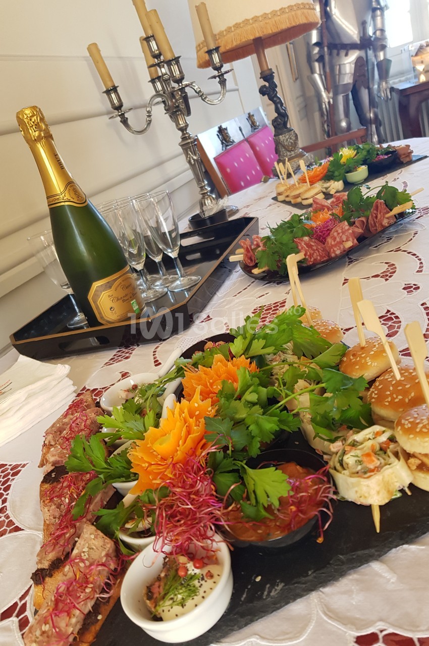 Plateau de mets variés avec charcuteries, légumes, mini-burgers et bouteille de champagne sur une table décorée.