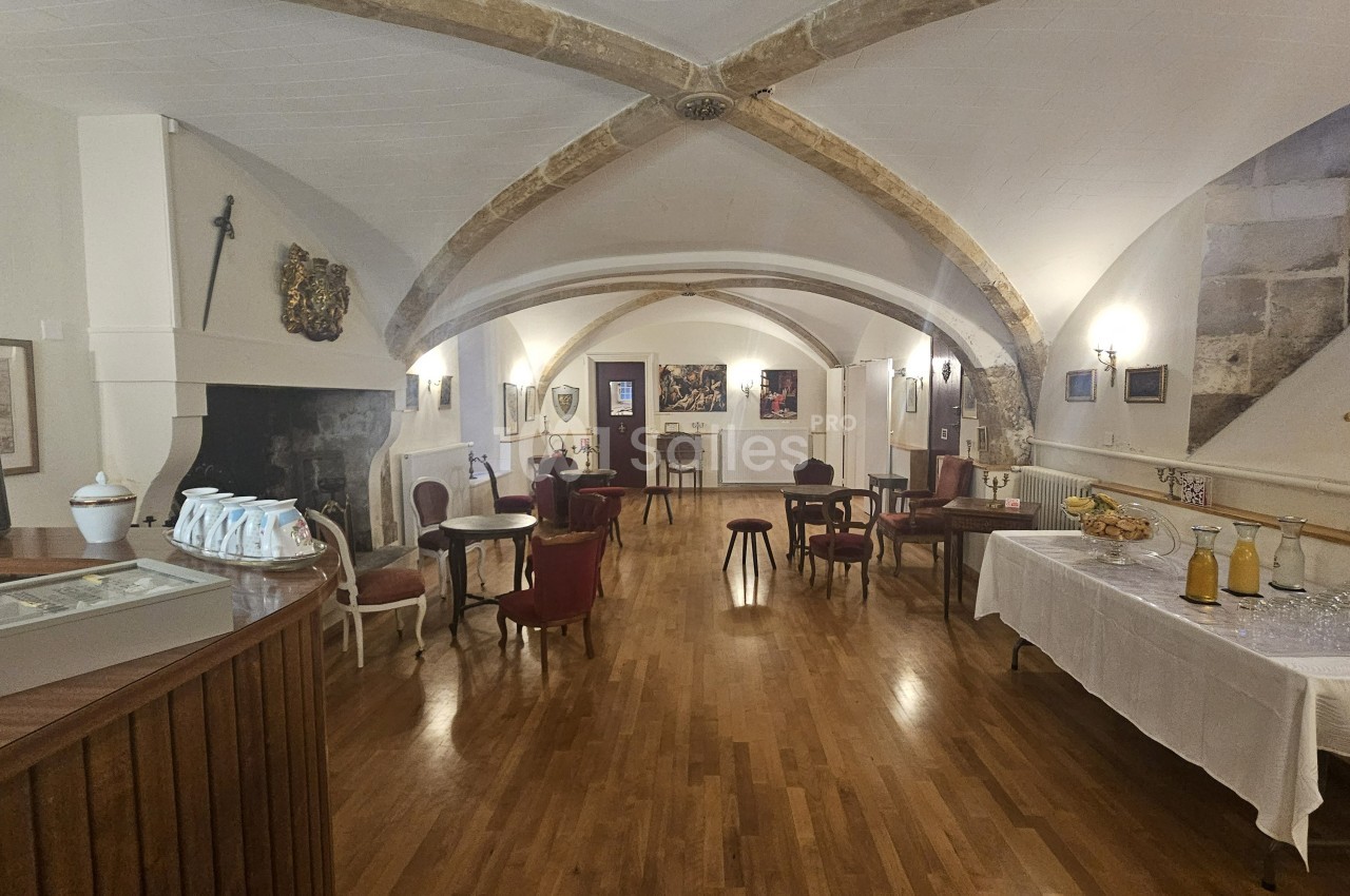 Salle voûtée avec parquet, tables et chaises, buffet dressé à droite et cheminée décorative à gauche.