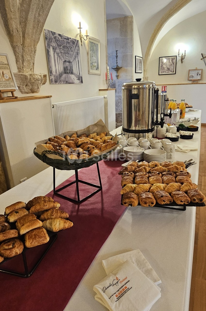 Buffet de petit-déjeuner avec viennoiseries, boissons chaudes, jus de fruits et serviettes sur une table dans une salle…