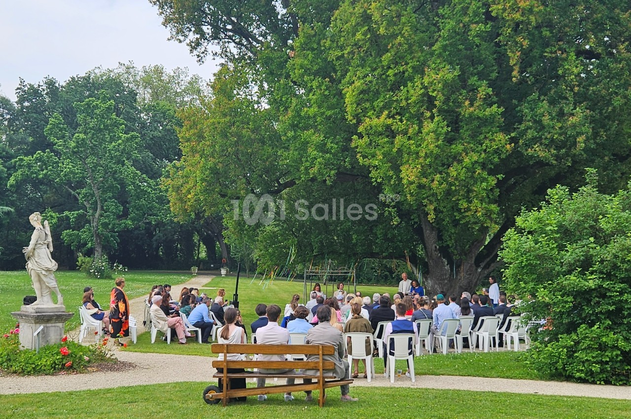 Un groupe de personnes assises en plein air dans un parc verdoyant, près d'une grande statue et d'un arbre imposant.