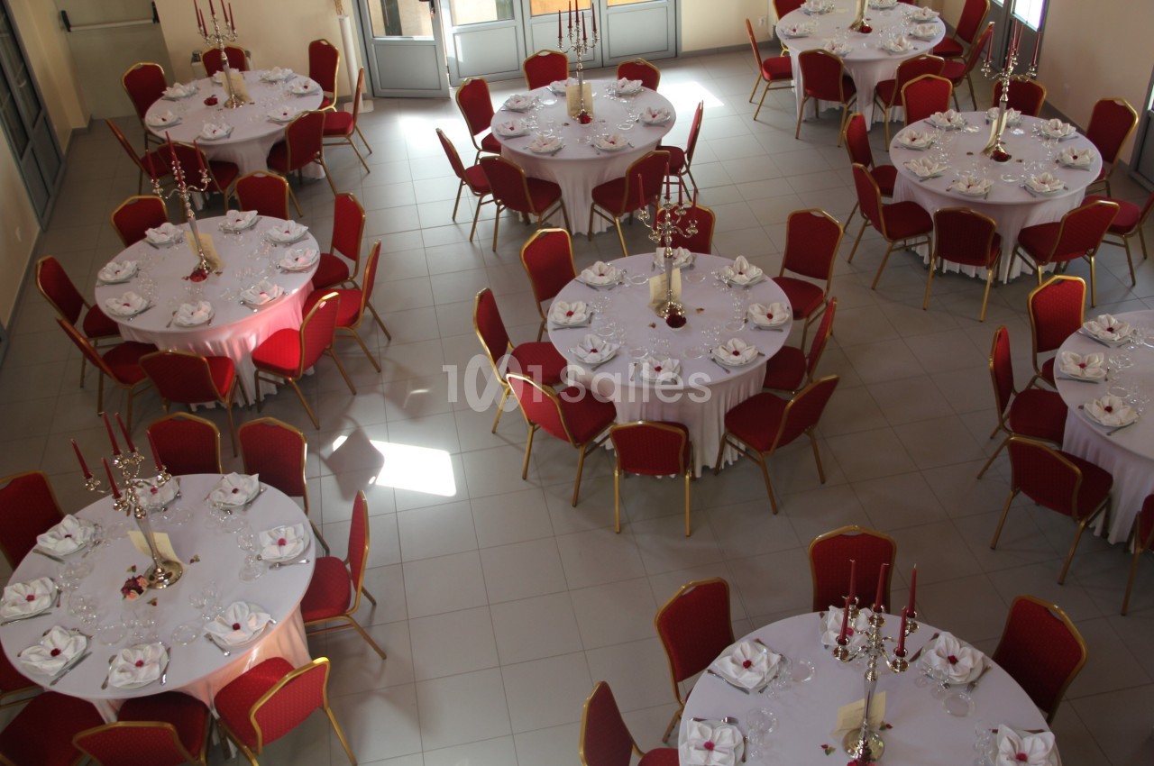 Salle de réception avec des tables rondes dressées, nappes blanches, chaises rouges et décorations de centre de table.