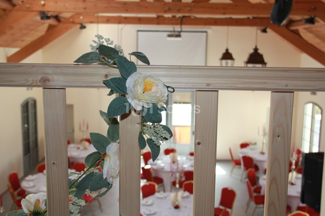 Fleurs décoratives accrochées à une rambarde en bois, avec une salle de réception lumineuse en arrière-plan.