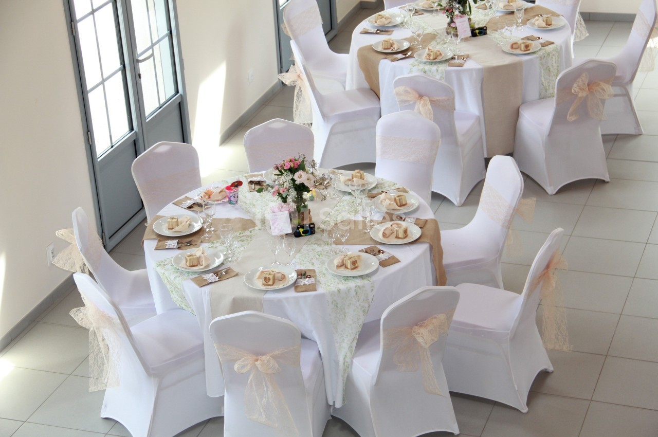 Tables rondes décorées avec nappes blanches, centres de table floraux et chaises ornées de nœuds en ruban beige.