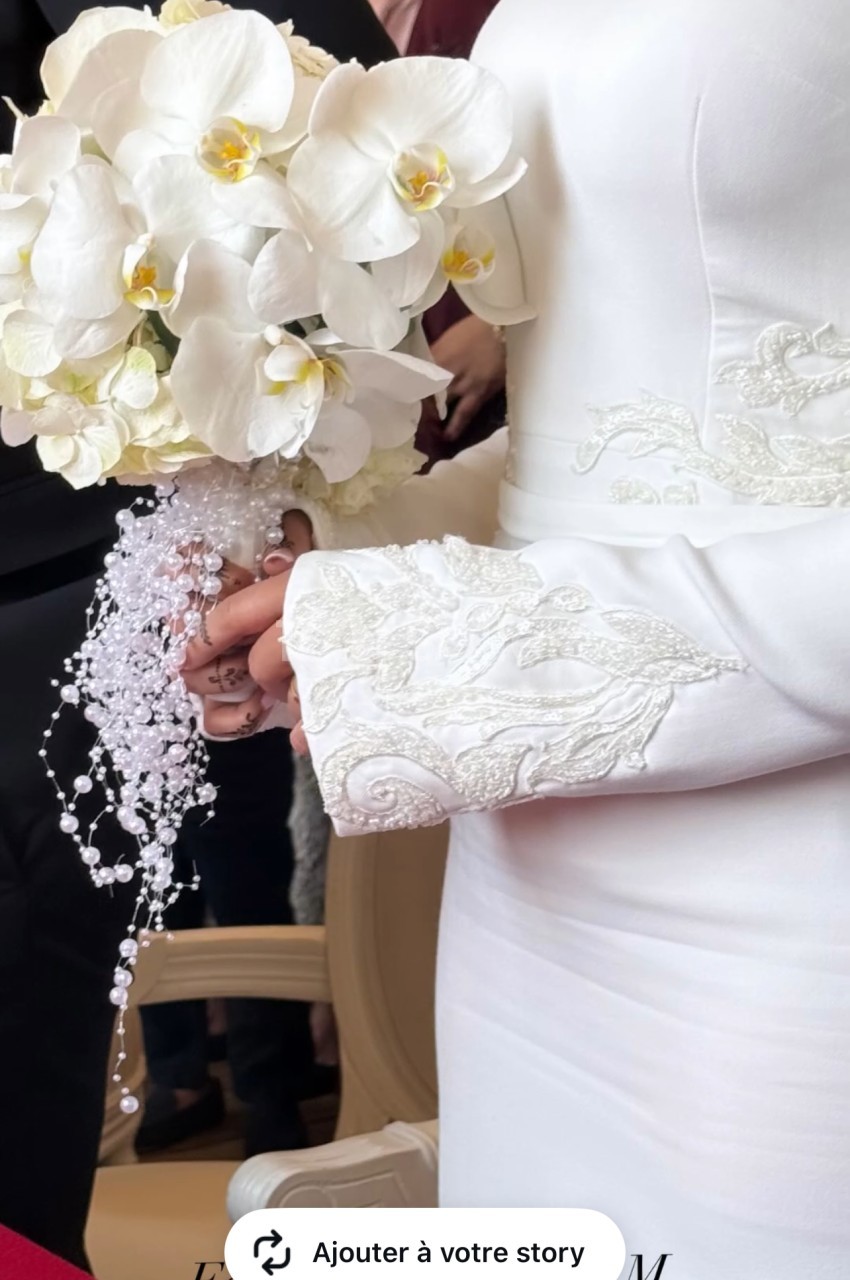 Une mariée en robe blanche tient un bouquet d'orchidées blanches avec des perles décoratives.