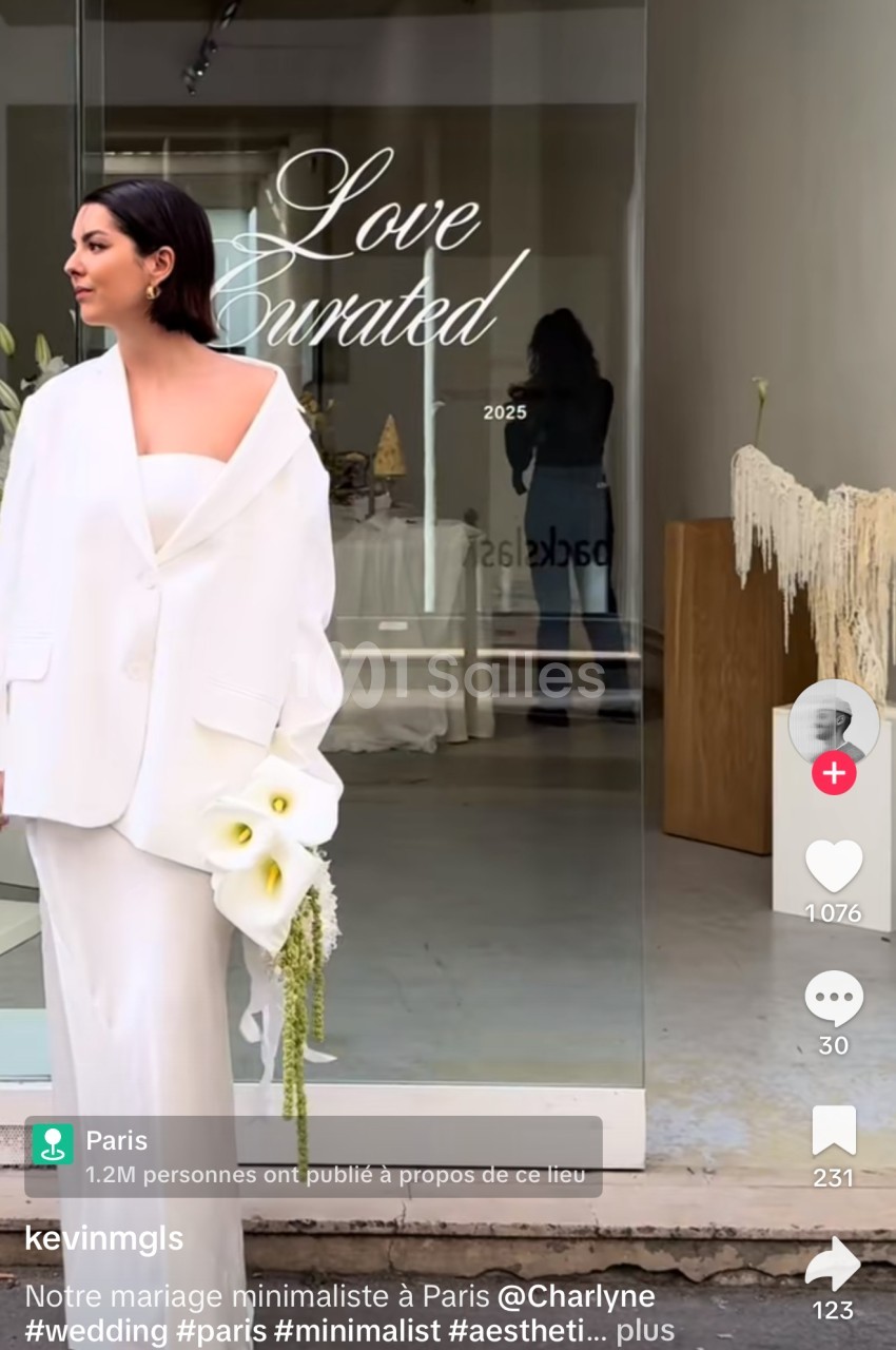 Une mariée en tailleur blanc tenant un bouquet devant une vitrine avec l'inscription ’Love Curated’.