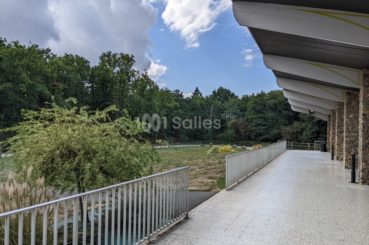 Terrasse couverte avec garde-corps donnant sur un espace vert arboré sous un ciel partiellement nuageux.