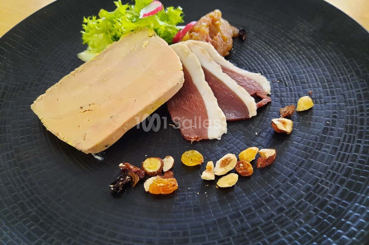 Assiette composée de foie gras, magret de canard fumé, fruits secs, chutney et salade verte sur une assiette noire.