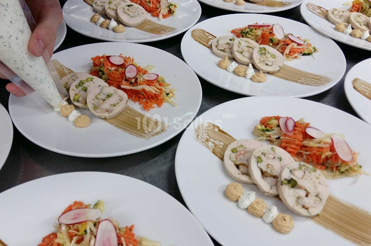 Assiettes dressées avec des roulés de volaille, légumes râpés et décorations de sauce, en préparation en cuisine.