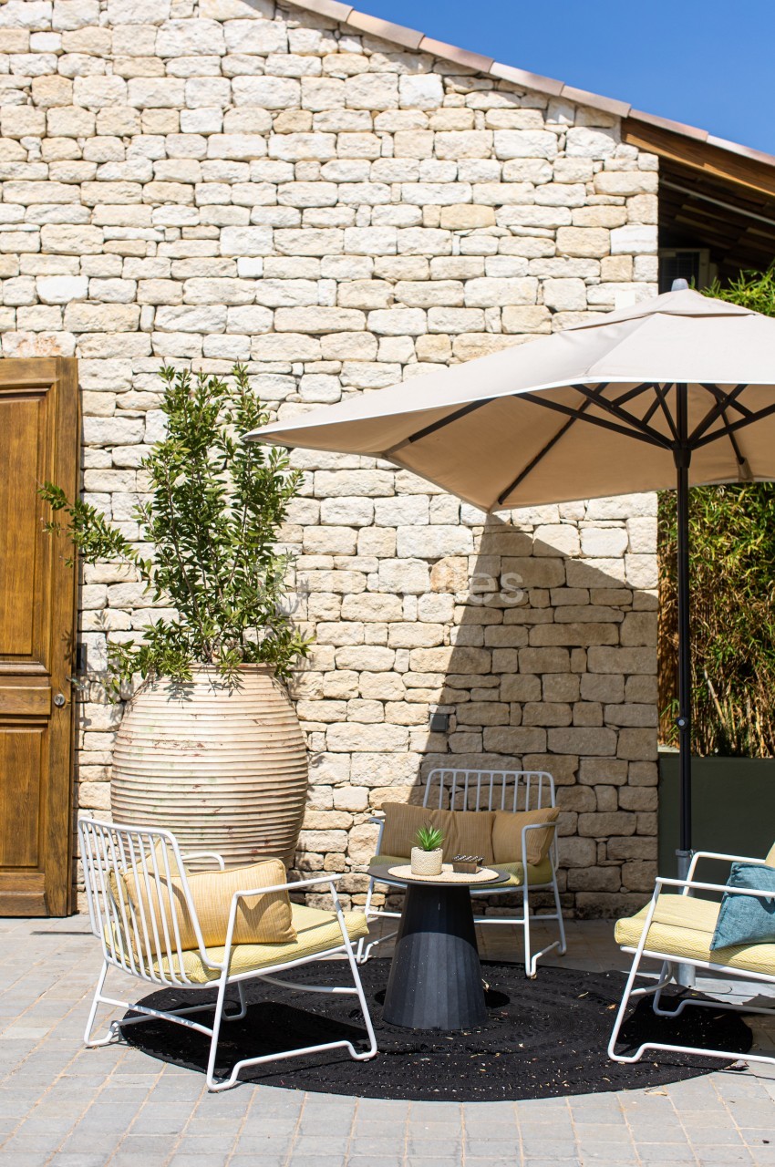 Mobilier de jardin avec fauteuils, table basse et parasol beige, disposés sur une terrasse en pierre devant un mur en pierre…