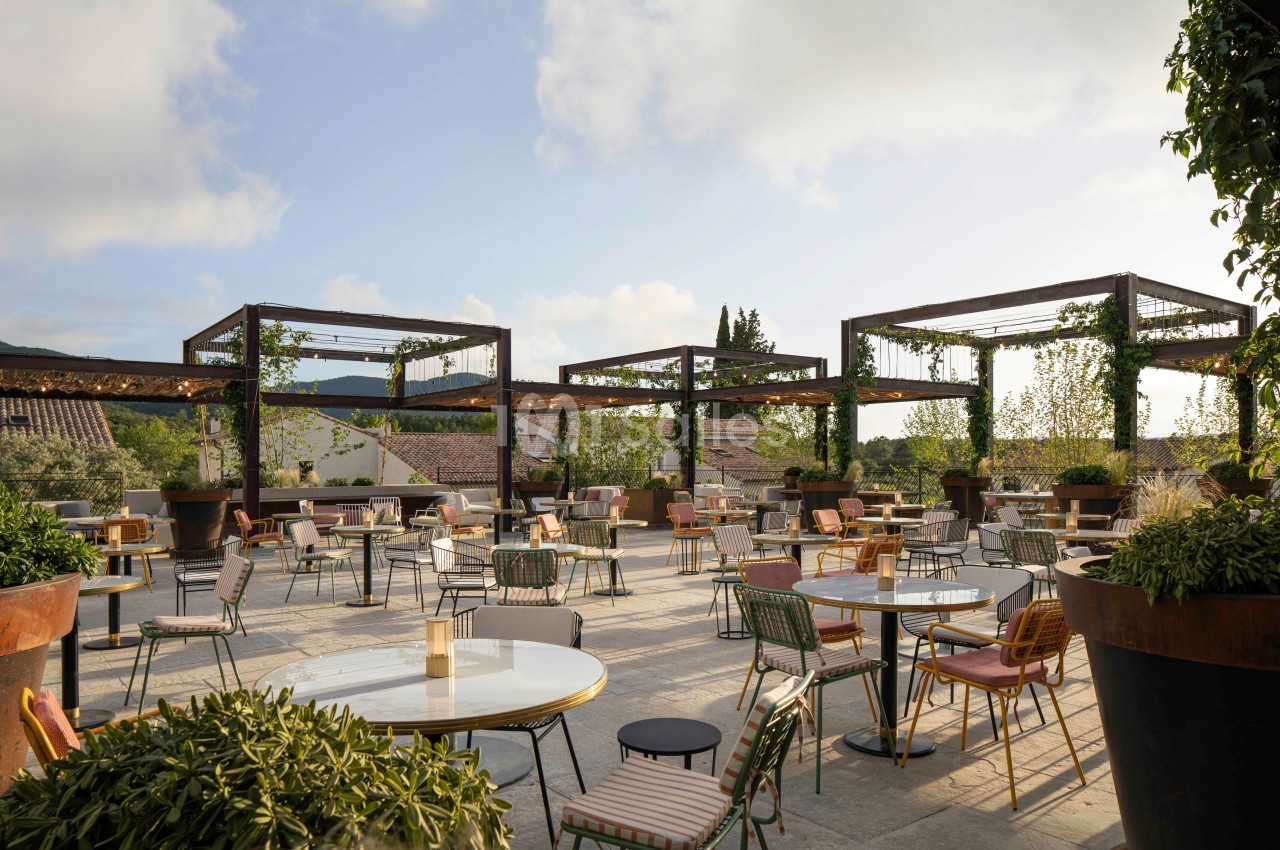 Terrasse extérieure aménagée avec des tables et des chaises, entourée de plantes et de structures en bois.