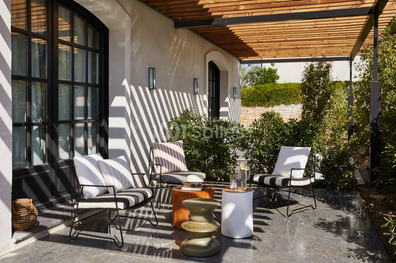Terrasse ombragée avec mobilier de jardin moderne, coussins rayés, tables d'appoint et plantes environnantes.