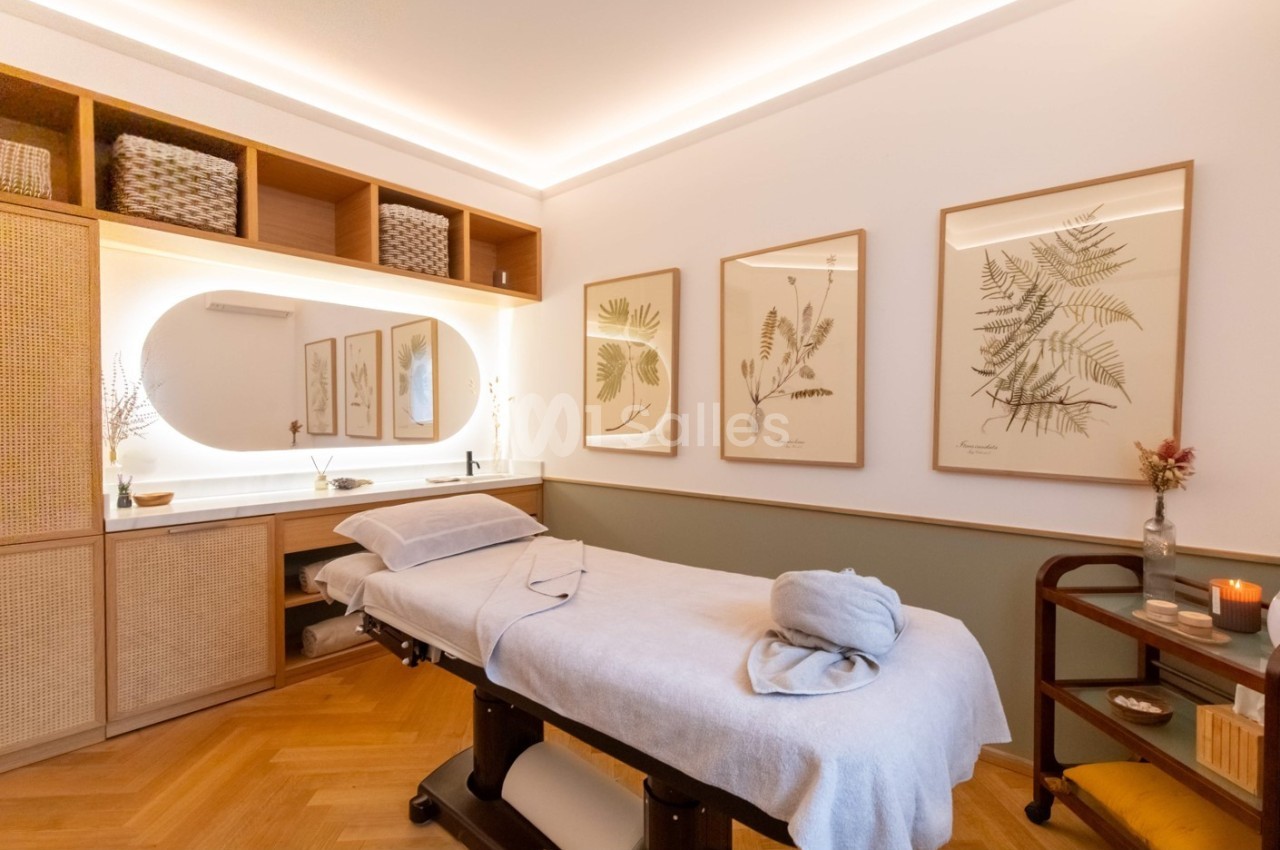Salle de massage lumineuse avec table de soin, décorations murales végétales et éclairage chaleureux.