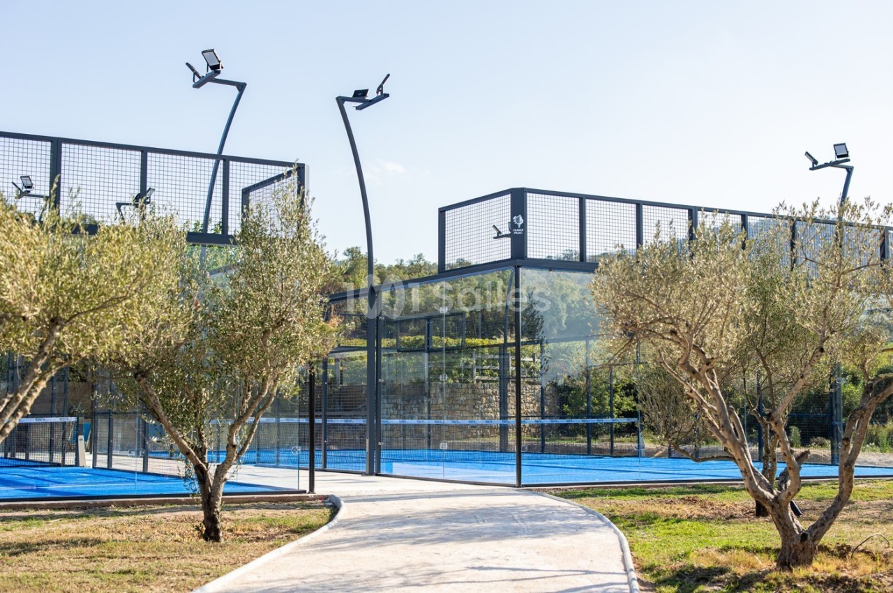 Terrains de padel extérieurs entourés d'arbres et éclairés par des lampadaires, avec un chemin en premier plan.