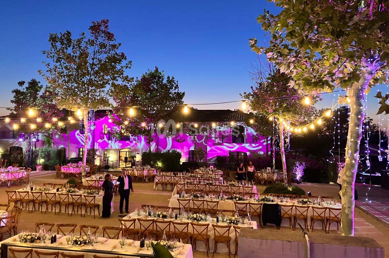 Terrasse décorée pour un événement en soirée, avec guirlandes lumineuses, tables dressées et éclairages colorés.