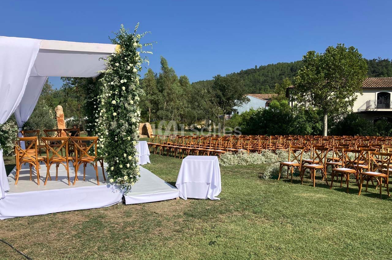 Cérémonie de mariage en plein air avec une arche fleurie, des chaises en bois et un paysage verdoyant en arrière-plan.