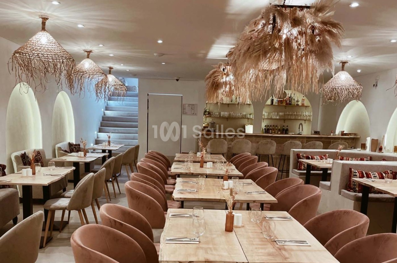 Salle de restaurant lumineuse avec tables en bois, chaises rembourrées et décorations suspendues en fibres naturelles.
