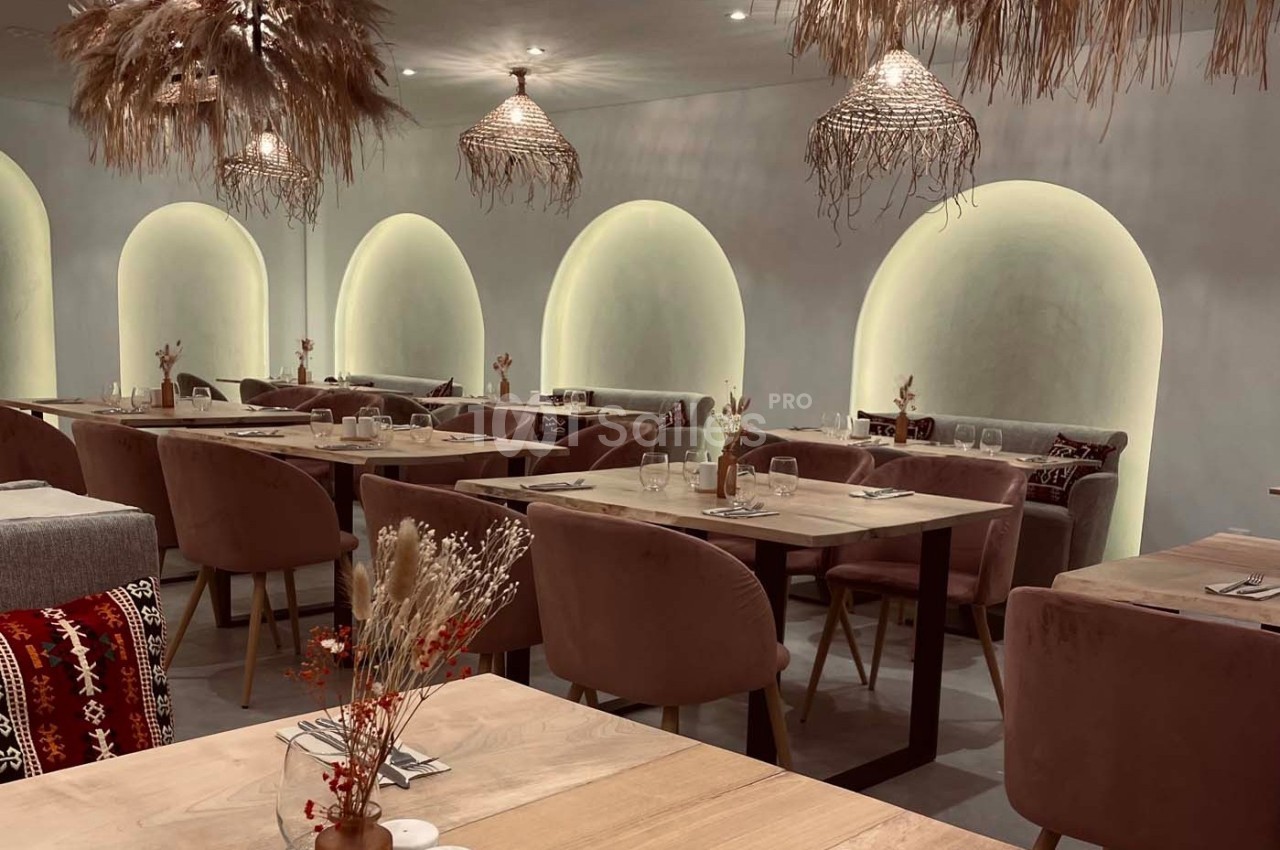 Salle de restaurant avec tables en bois, chaises rembourrées, arches lumineuses et décorations en fibres naturelles.