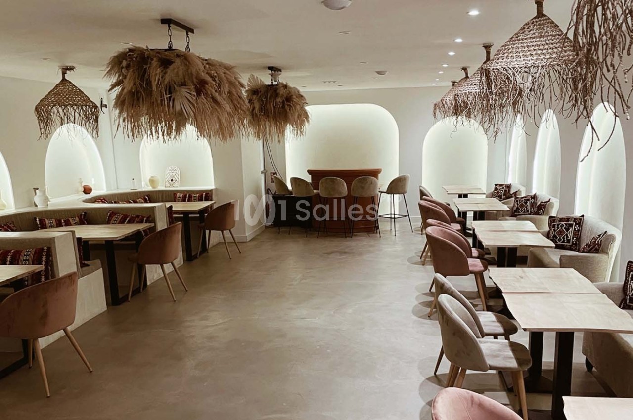 Salle de restaurant lumineuse avec tables en bois, chaises rembourrées et décorations suspendues en fibres naturelles.