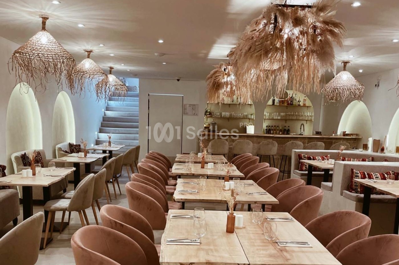 Salle de restaurant lumineuse avec tables en bois, chaises rembourrées et suspensions décoratives en fibres naturelles.